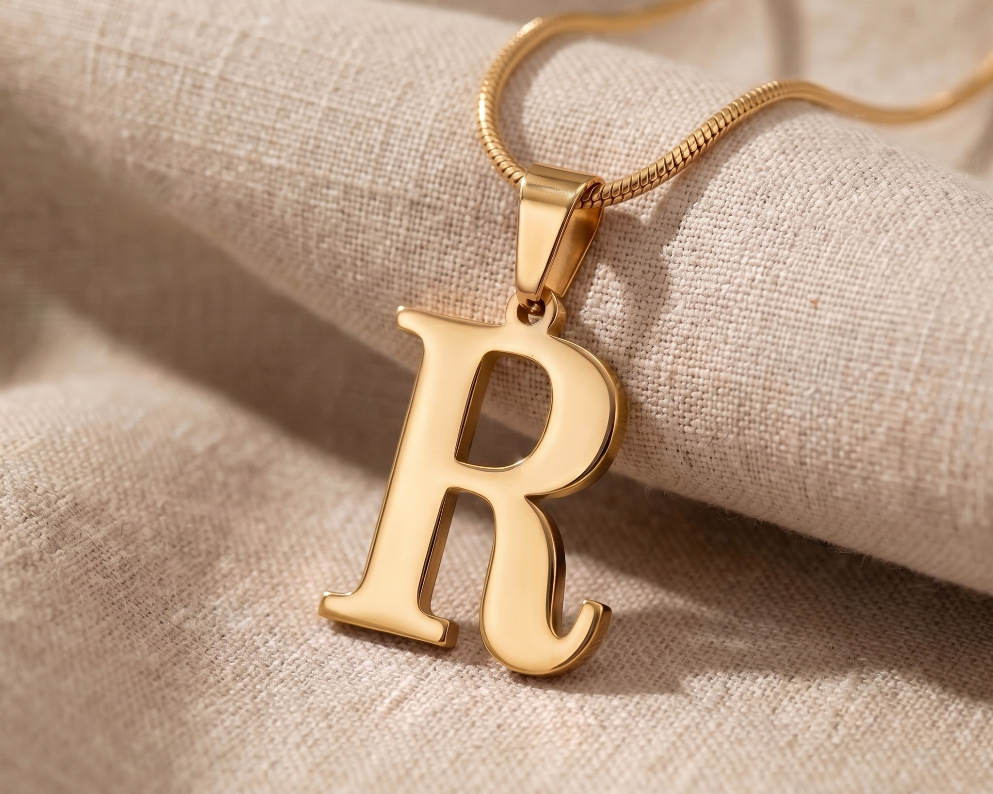 A small initial pendant resting against a plain neutral top