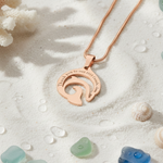 Rose gold dolphin necklace with engraved message on sandy background, belle fever resilience and empowerment pendant.