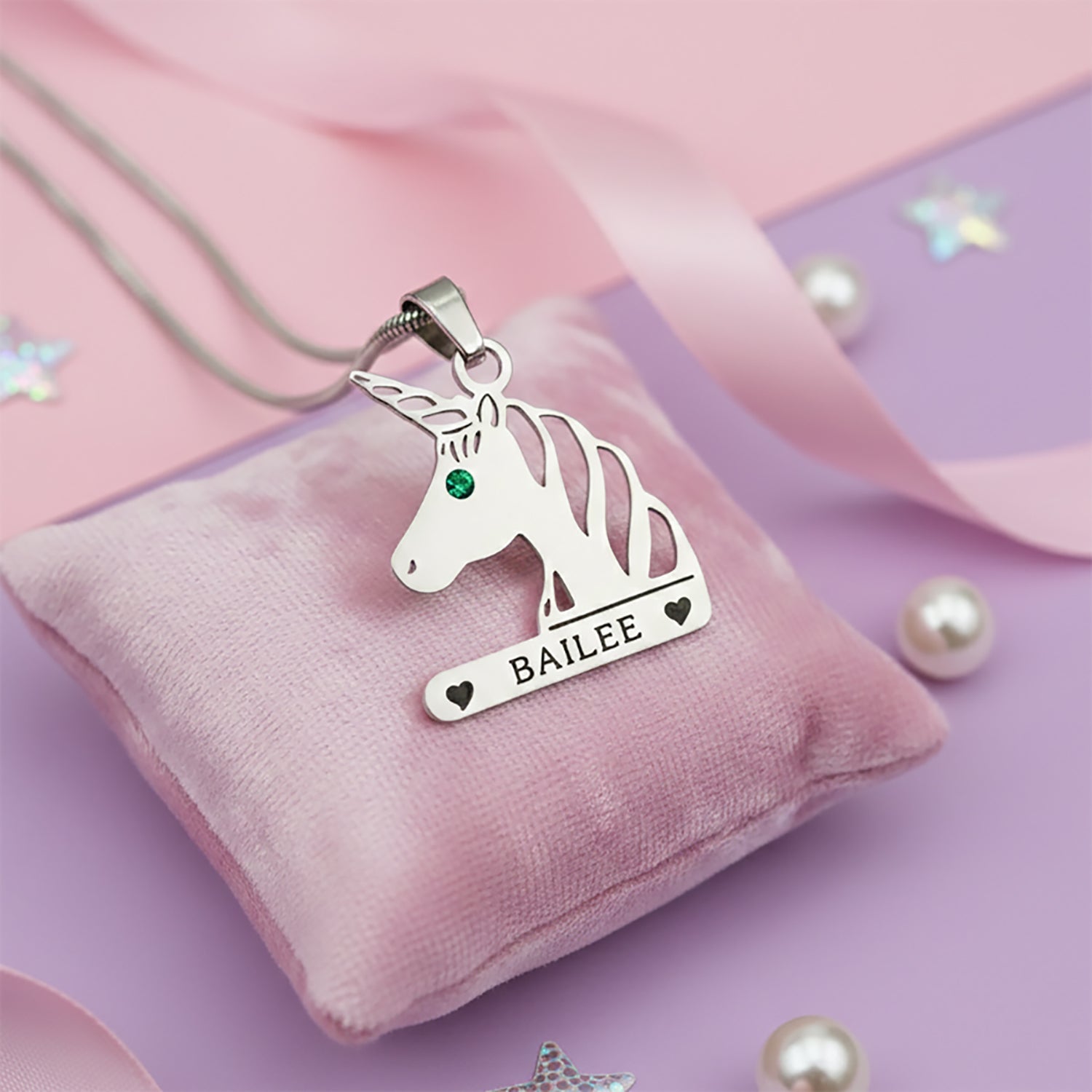 Unicorn head necklace with birthstone and custom engraved name in silver finish on pink background.