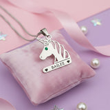 Unicorn head necklace with birthstone and custom engraved name in silver finish on pink background.