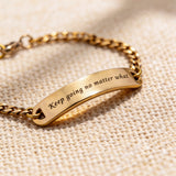 Gold bar bracelet with engraved plate displayed on neutral fabric background