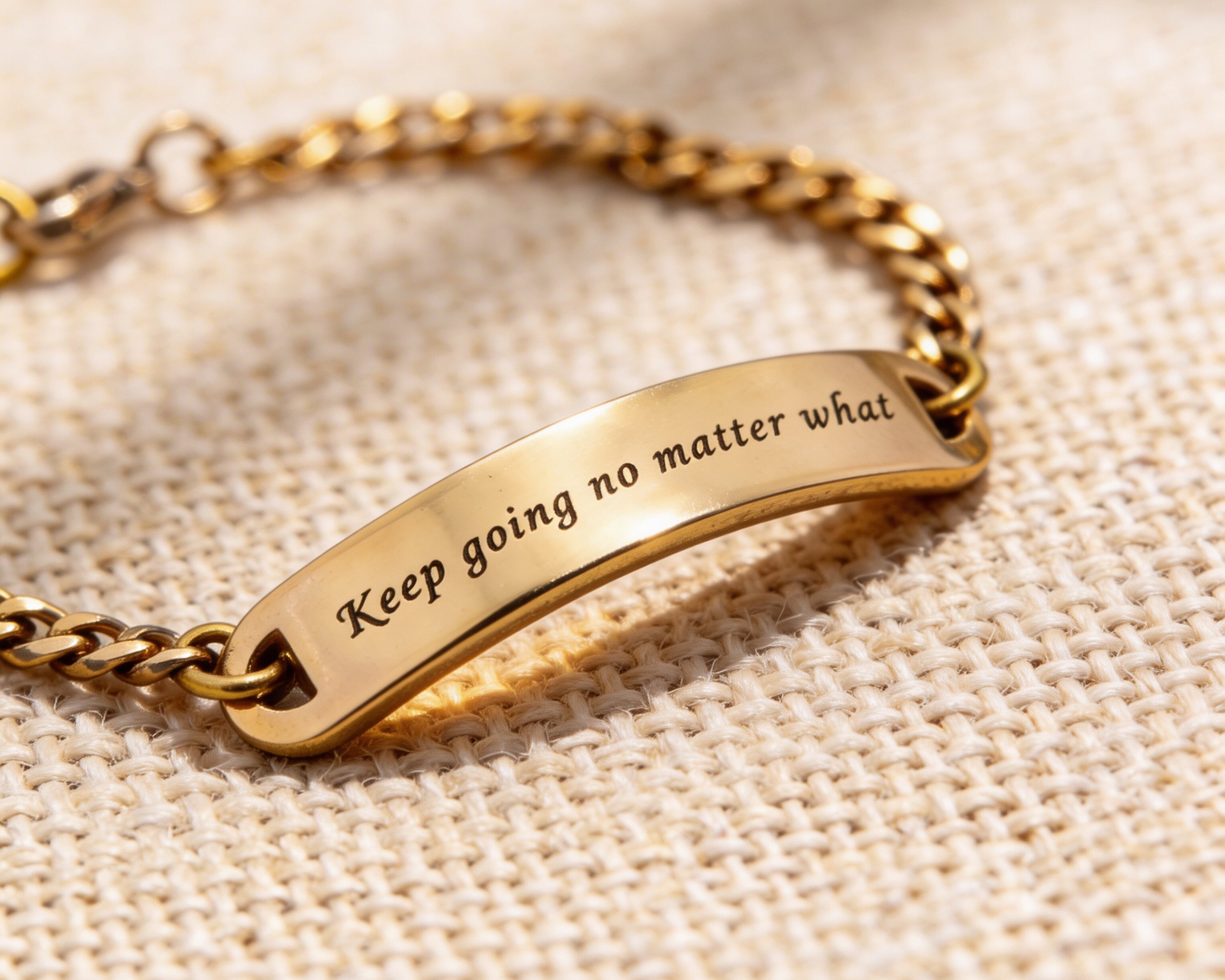 Gold bar bracelet with engraved plate displayed on neutral fabric background