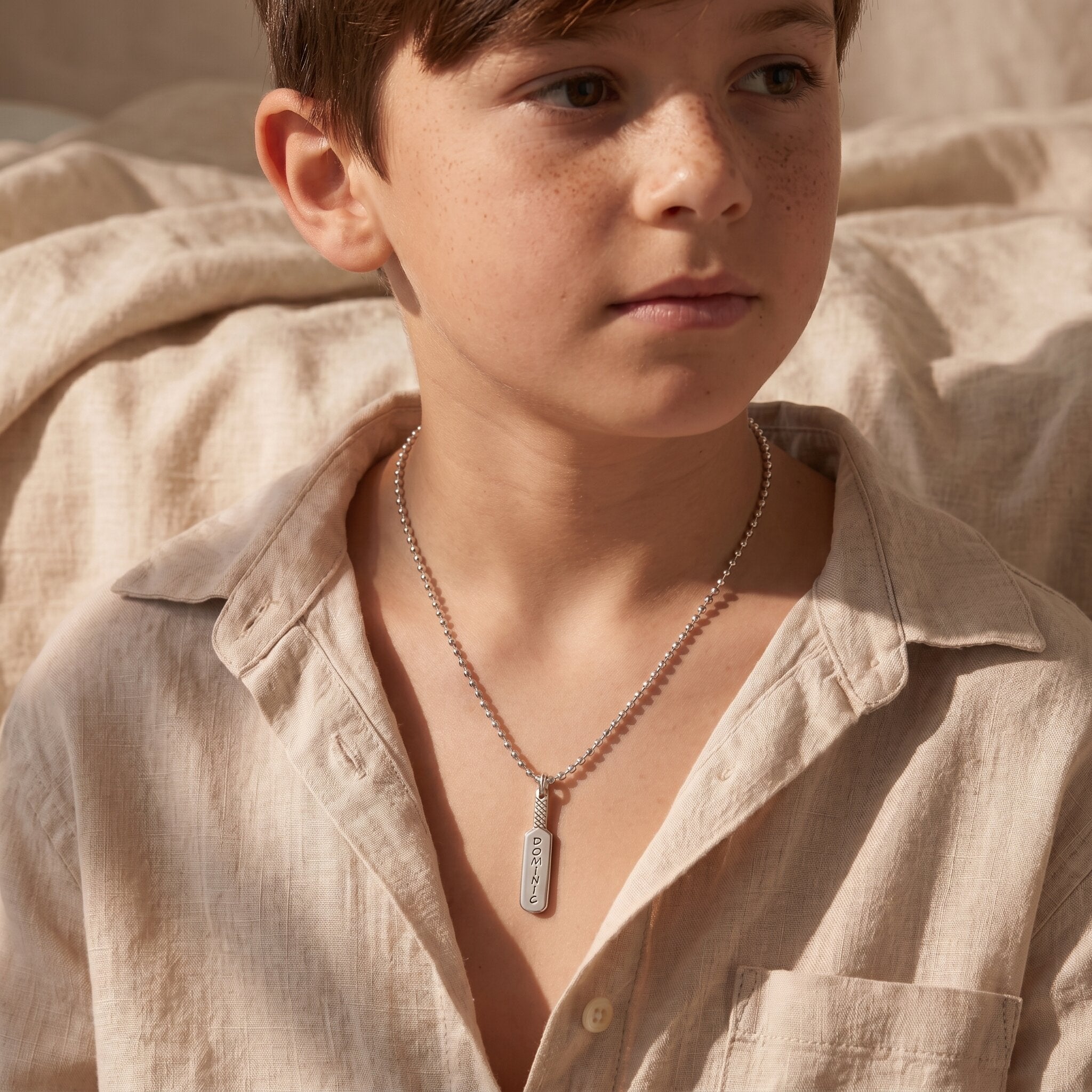 A model wearing cricket bat name necklace with engraved pendant, sporty personalised style