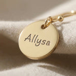 Close up of personalised earrings showing engraved name detail on round disc