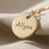 Close up of personalised earrings showing engraved name detail on round disc
