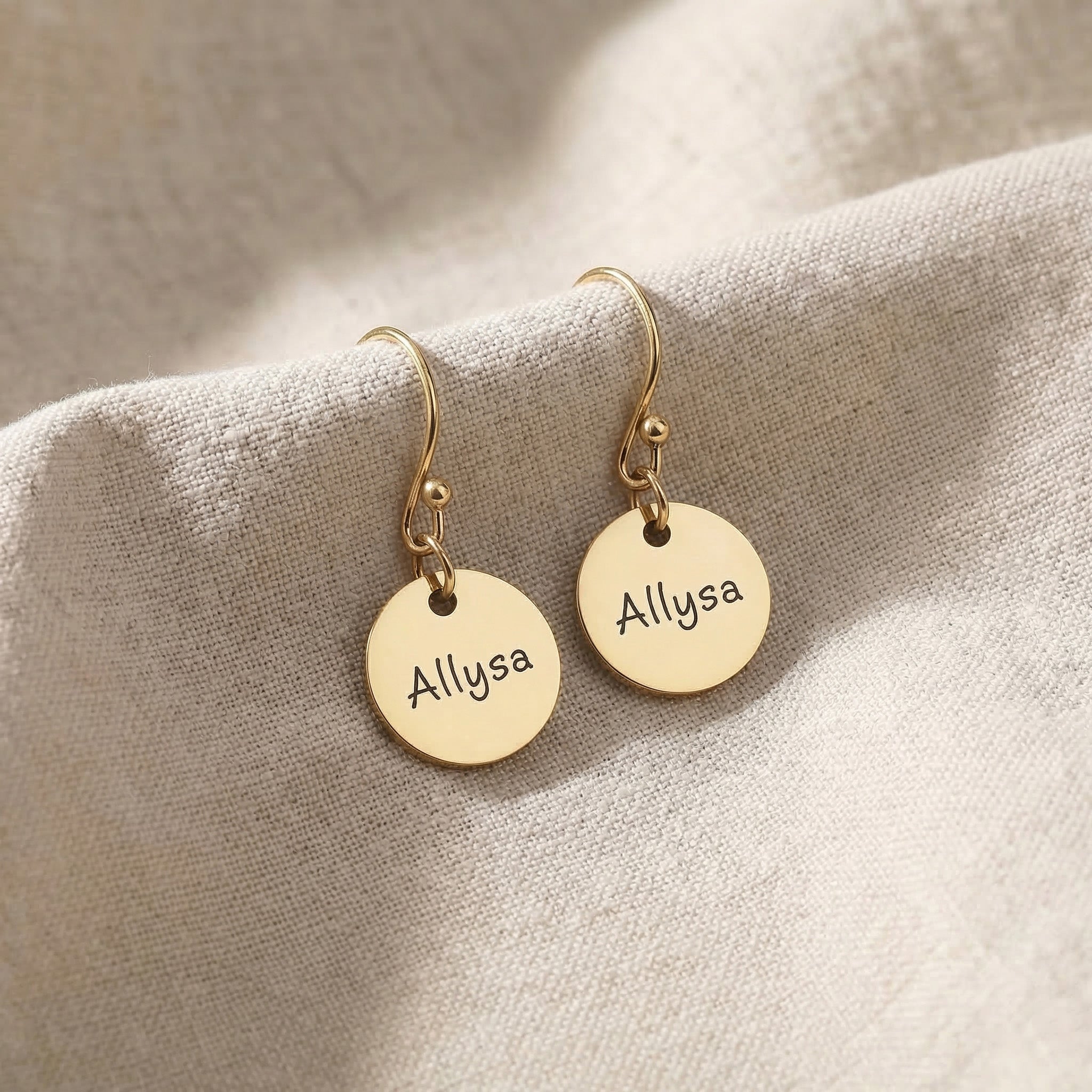 Gold personalised earrings with engraved name on disc design displayed on neutral background