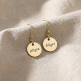 Gold personalised earrings with engraved name on disc design displayed on neutral background